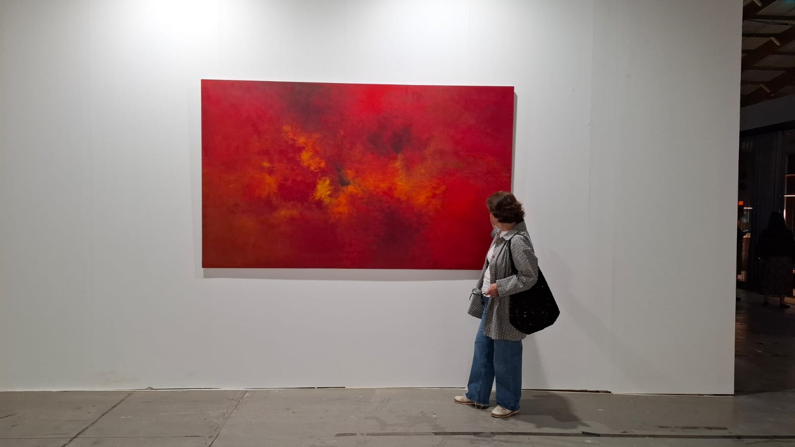Rojo, pero con modales, obra abstracta en tonos rojos y naranjas, presentada en Marbella, con la artista junto a la obra mostrando su escala.
